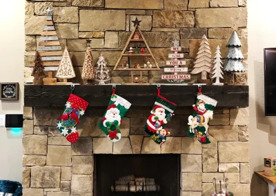 Stone Fireplace Mantle decorated with wooden Christmas trees and handmade stockings